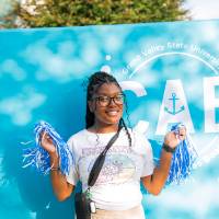 student posing in front of CAB backdrop at Laker Kickoff photo booth with pom poms